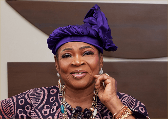 Recent portrait of Queen Salawa Abeni smiling in a purple gele and patterned buba